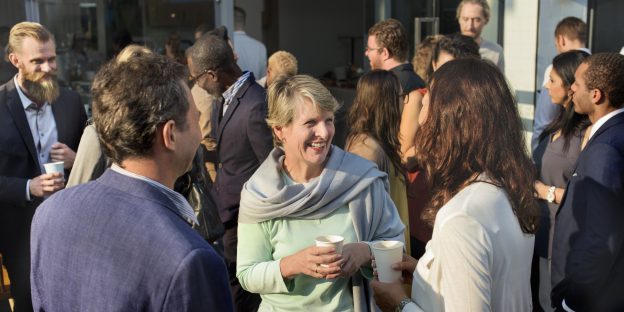 een groep mensen met elkaar in gesprek en een koffiebeker in de hand