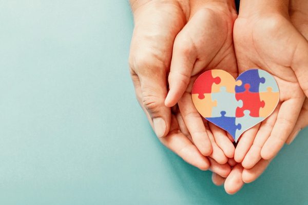Adult and chiild hands holding jigsaw puzzle heart shape, Autism